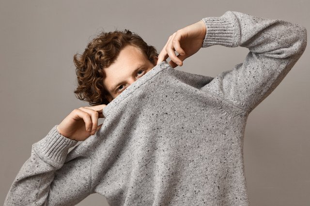 portrait-trendy-looking-cute-young-caucasian-male-with-wavy-voluminous-curly-hairstyle-fooling-around-pulling-gray-sweater-his-face-leaving-eyes-open-having-confident-facial-expression.jpg